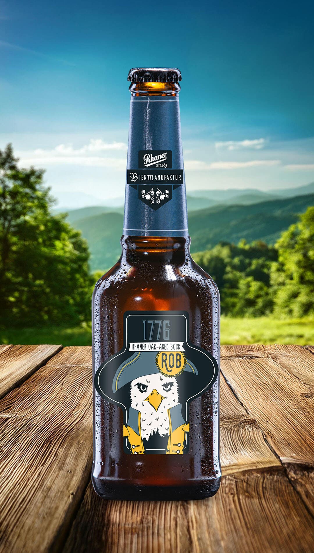 Eine Flasche Rhaner "1776 Oak-Aged Bock" (ROB) Biermanufaktur mit dunkelblauer Halsbanderole und einer Illustration eines Adlers in historischer Uniform auf dem Etikett auf einem Holztisch vor einer grünen Hügellandschaft