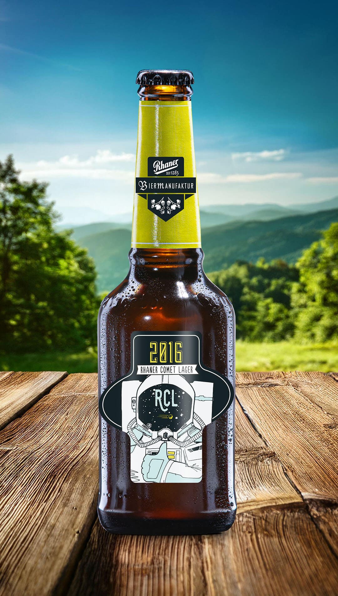 Eine Flasche Rhaner Comet Lager (2016) Biermanufaktur mit gelber Halsbanderole und einem Astronauten-Motiv auf dem dunklen Etikett auf einem Holztisch vor einer grünen Hügellandschaft