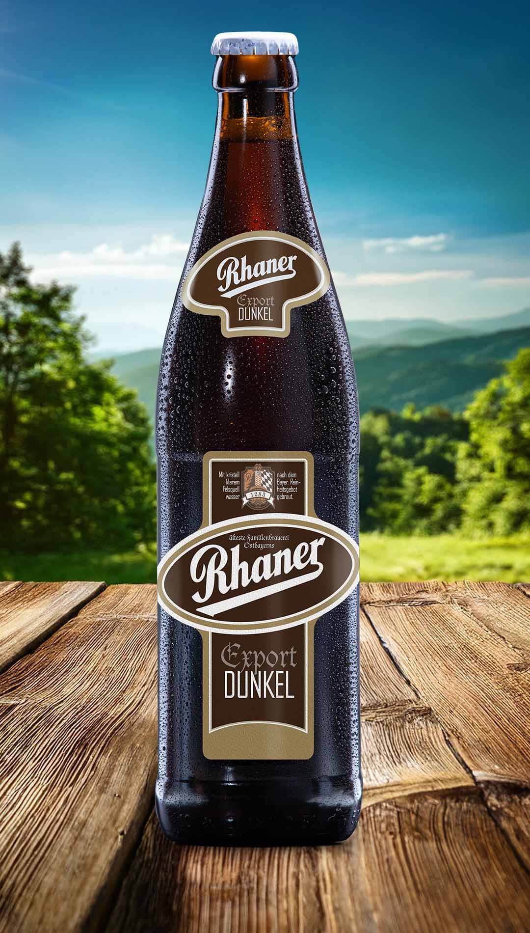 Eine Flasche Rhaner Export Dunkel mit braun-beigem Etikett auf einem Holztisch vor einer grünen Hügellandschaft