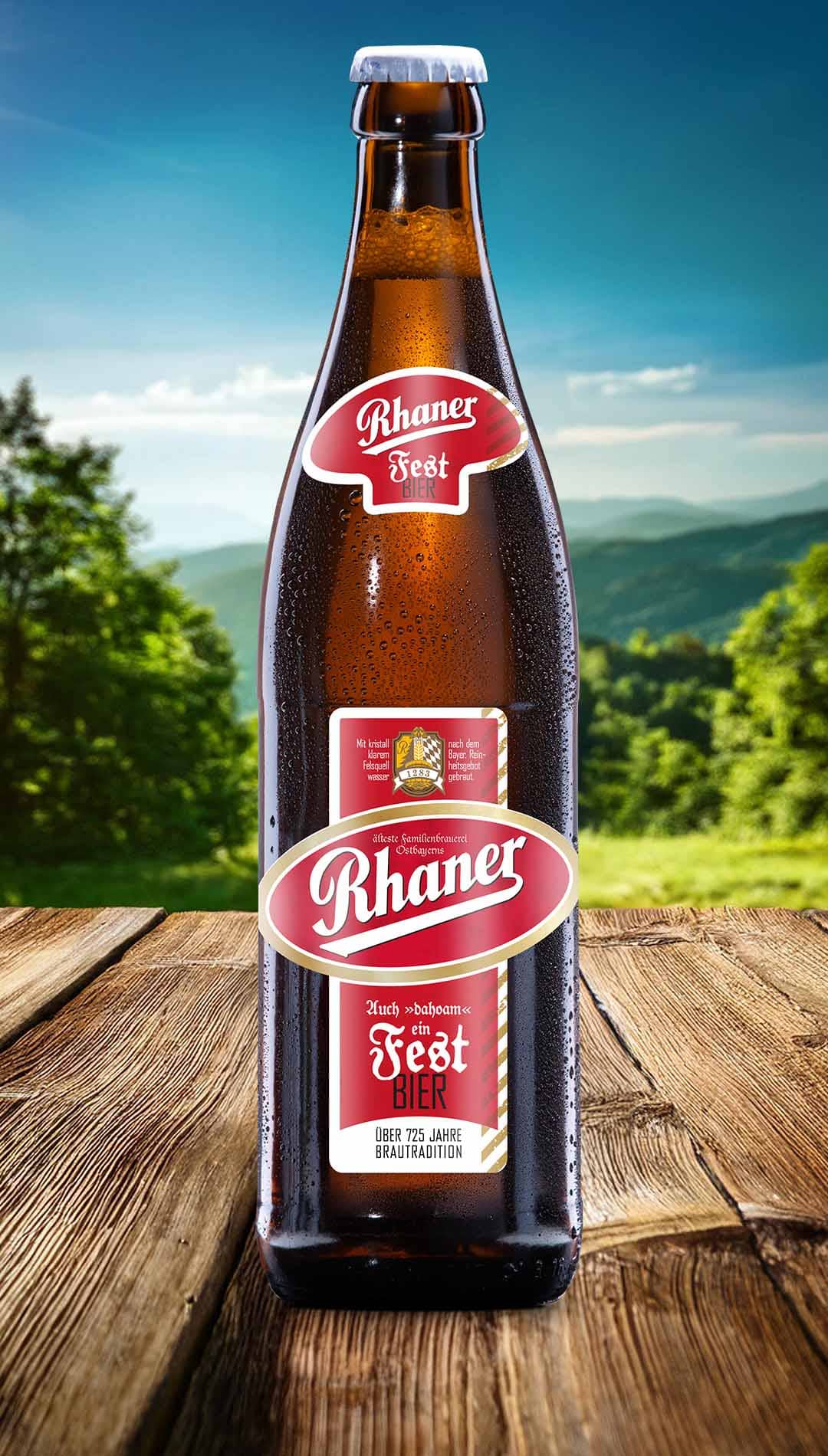 Eine Flasche Rhaner Festbier mit rot-weißem Etikett und der Aufschrift "Auch dahoam ein Festbier" auf einem Holztisch vor einer grünen Hügellandschaft