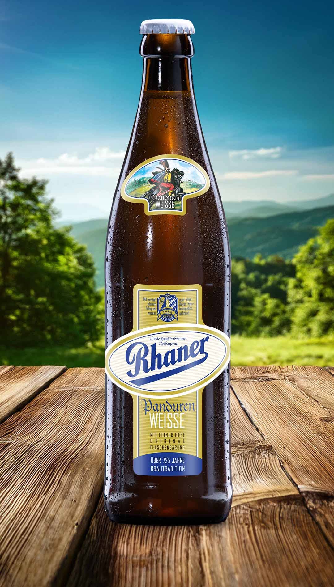 Eine Flasche Rhaner Panduren Weisse mit gold-weißem Etikett und Reiter-Motiv auf einem Holztisch vor einer grünen Hügellandschaft