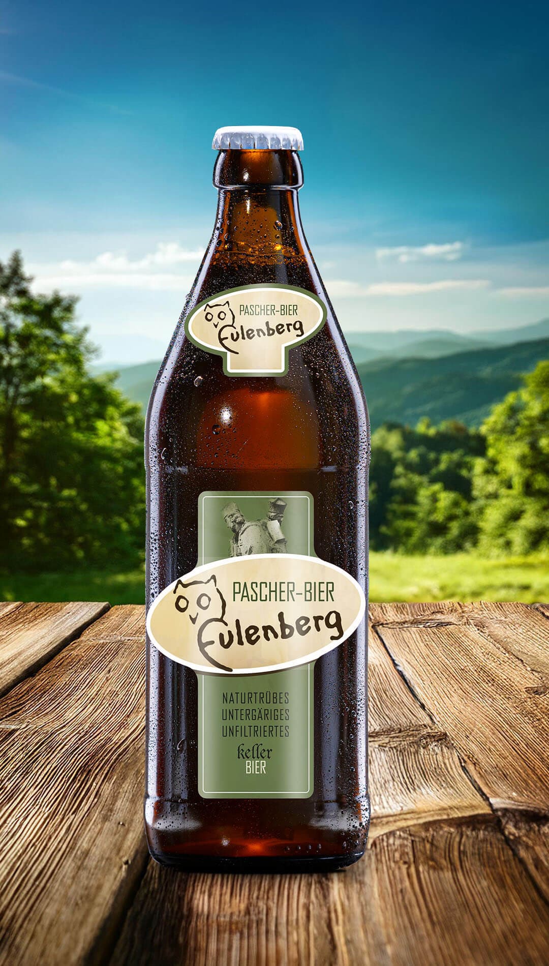 Eine Flasche Pascher-Bier Eulenberg naturtrübes Kellerbier mit Eulen-Logo auf einem Holztisch vor einer grünen Hügellandschaft