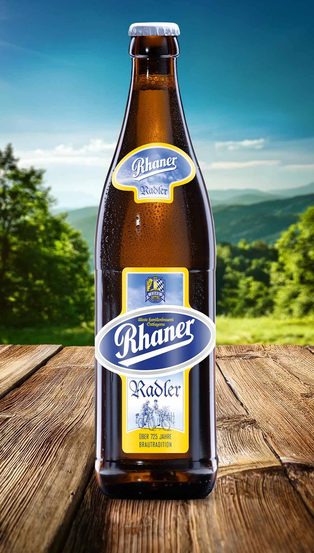 Eine Flasche Rhaner Radler mit blau-gelbem Etikett und Fahrrad-Motiv auf einem Holztisch vor einer grünen Hügellandschaft